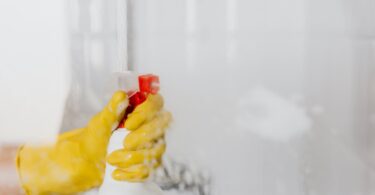 person in glove spraying detergent at walk in shower glass